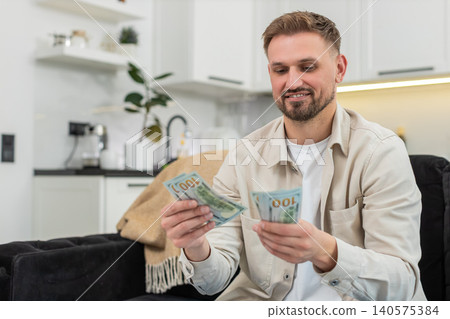 Young man counts cash dollars smiles happy with savings plans dream purchase investment bonus salary Young man counts cash dollars smiles happy with savings plans dream purchase investment bonus salary 140575384