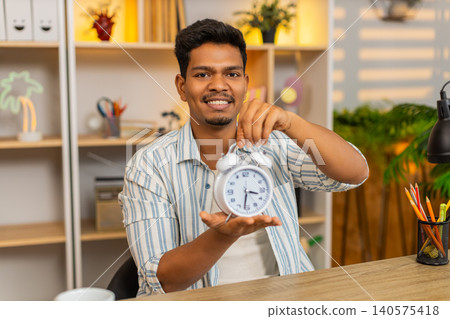 Indian man on home table showing clock to camera while speaking during work in cozy home living room 140575418
