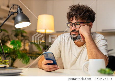 Arabian man bored scrolls smartphone news at night stressed demotivated sighs needs break from news Arabian man bored scrolls smartphone news at night stressed demotivated sighs needs break from news 140575423