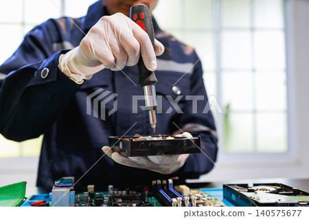 Technician in gloves repairs a computer hard drive with a screwdriver over an open motherboard in a bright workshop, showing data recovery, maintenance and hardware service. Technician in gloves repairs a computer hard drive with a screwdriver over an open motherboard in a bright workshop, showing data recovery, maintenance and hardware service. 140575677