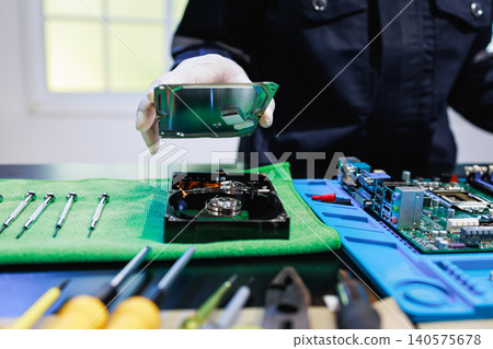 Technician in gloves holding a hard drive cover above an open disk on a workbench with screwdrivers and circuit boards, showing data recovery, repair and computer maintenance. Technician in gloves holding a hard drive cover above an open disk on a workbench with screwdrivers and circuit boards, showing data recovery, repair and computer maintenance. 140575678