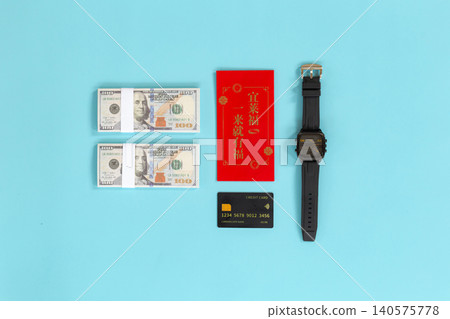 Bright blue background holds symbolic items. Red envelope suggests celebration or fortune. Stacked bills imply financial gain or reward. Black watch signals time's value or urgency 140575778