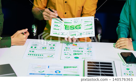 Business team reviewing esg charts and sustainability reports at a meeting table with a solar panel sample and phone, showing green finance, planning and corporate responsibility. Business team reviewing esg charts and sustainability reports at a meeting table with a solar panel sample and phone, showing green finance, planning and corporate responsibility. 140576363