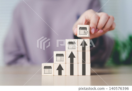 Franchise business growth and expansion concept. Hand stacking wooden blocks with store and arrow icons, franchise business growth, expansion, success entrepreneurship, market development, online shop Franchise business growth and expansion concept. Hand stacking wooden blocks with store and arrow icons, franchise business growth, expansion, success entrepreneurship, market development, online shop 140576396