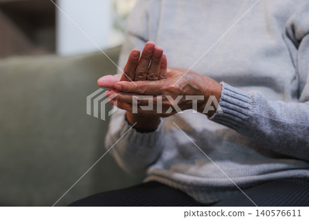 Close-up of an older adult rubbing hands while sitting indoors, showing dry skin, discomfort, self care, aging, and a quiet home setting. Close-up of an older adult rubbing hands while sitting indoors, showing dry skin, discomfort, self care, aging, and a quiet home setting. 140576611