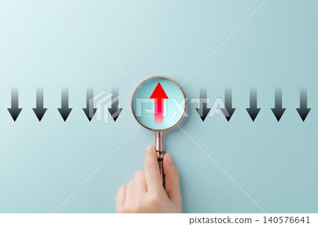 Thinking differently and finding new perspectives. A Hand holding magnifying glass reveals a red upward arrow among black downward arrows, innovation, leadership, unique thinking, and problem-solving. Thinking differently and finding new perspectives. A Hand holding magnifying glass reveals a red upward arrow among black downward arrows, innovation, leadership, unique thinking, and problem-solving. 140576641