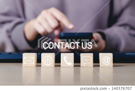 Contact Us and customer support concept. A person using a smartphone with wooden blocks contact icons, email, phone, chat, and web represents customer service, communication, and support assistance. Contact Us and customer support concept. A person using a smartphone with wooden blocks contact icons, email, phone, chat, and web represents customer service, communication, and support assistance. 140576707