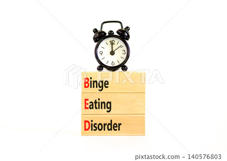 BED binge eating disorder symbol. Concept words BED binge eating disorder on beautiful wooden blocks. Beautiful white background. Alarm clock. Medical BED binge eating disorder concept. Copy space. BED binge eating disorder symbol. Concept words BED binge eating disorder on beautiful wooden blocks. Beautiful white background. Alarm clock. Medical BED binge eating disorder concept. Copy space. 140576803