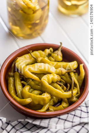 Pickled Yellow Banana Peppers in Terracotta Bowl With Jars on White Table, Tangy Appetizer 140576904
