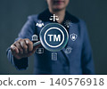 TM, Trademark Protection, Intellectual Property Concept. Person holding magnifying glass with "TM" symbol, icons of intellectual property, legal, patents, security, copyright, registered trademark, 140576918