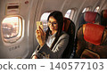 Young Caucasian woman smiling while using her smartphone inside an airplane cabin 140577103