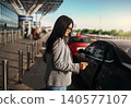 Hispanic young adult businesswoman using smartphone next to taxi outside airport terminal 140577107