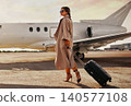 Elegant Caucasian mid adult woman walking with suitcase on airport runway by private jet 140577108
