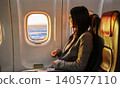 Happy young adult Asian woman smiling and looking out the window inside airplane cabin 140577110