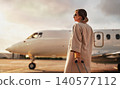 Mature caucasian woman holding suitcase standing on airport tarmac near private jet 140577112