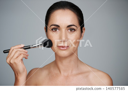Beauty, brush and portrait of woman in studio with makeup, natural and facial glow routine. Cosmetics, self care and confident mature female person with cosmetology tool isolated by gray background. Beauty, brush and portrait of woman in studio with makeup, natural and facial glow routine. Cosmetics, self care and confident mature female person with cosmetology tool isolated by gray background. 140577585