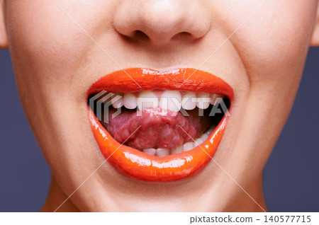 Beauty, lipstick and woman with tongue out, makeup and closeup of shiny cosmetic product with skin. Lick, flirting and orange lip gloss for aesthetic in studio with cosmetology on blue background Beauty, lipstick and woman with tongue out, makeup and closeup of shiny cosmetic product with skin. Lick, flirting and orange lip gloss for aesthetic in studio with cosmetology on blue background 140577715