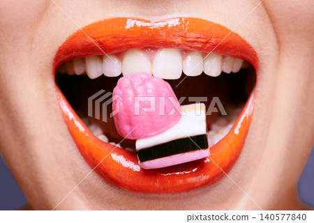 Beauty, lipstick and woman with sweets in mouth, makeup and creativity with closeup of shiny cosmetic product. Licorice, candy and orange lip gloss for aesthetic, art and cosmetology with glamour Beauty, lipstick and woman with sweets in mouth, makeup and creativity with closeup of shiny cosmetic product. Licorice, candy and orange lip gloss for aesthetic, art and cosmetology with glamour 140577840