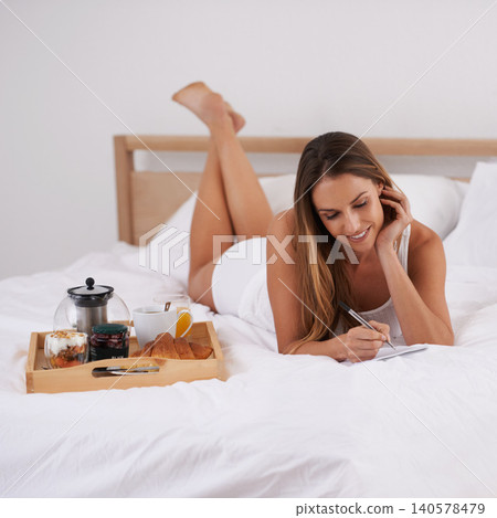 Woman, breakfast and bed with pen and notebook for relax, writing and plan in hotel or bedroom on weekend. Young person and smile with diary for notes in morning for wakeup on blanket with coffee 140578479