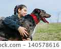 Girl with dark hair in blue hoodie hugs her dog outdoors 140578616