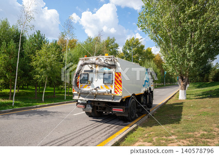 Road sweeper truck cleaning asphalt surface on city street. Industrial machine with rotating brush for pavement hygiene. Municipal service vehicle for urban maintenance and sanitation. Road sweeper truck cleaning asphalt surface on city street. Industrial machine with rotating brush for pavement hygiene. Municipal service vehicle for urban maintenance and sanitation. 140578796