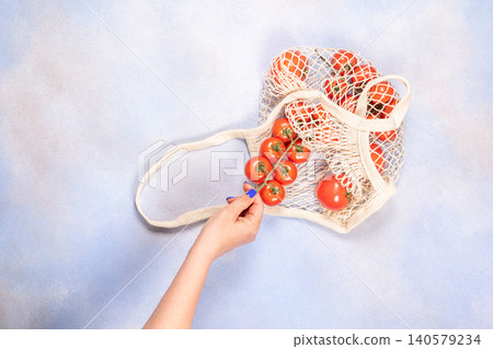 Hand holding cherry tomatoes from reusable mesh bag 140579234