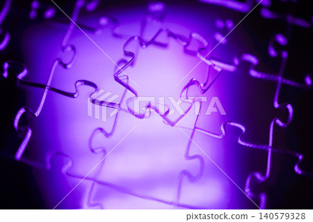 Close-up of interlocking puzzle pieces illuminated by purple light, showcasing intricate details and textures of the jigsaw puzzle against a blurred background Close-up of interlocking puzzle pieces illuminated by purple light, showcasing intricate details and textures of the jigsaw puzzle against a blurred background 140579328