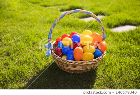 Colorful plastic Easter eggs in a woven basket resting on green grass under bright sunlight, perfect for spring celebrations and holiday activities Colorful plastic Easter eggs in a woven basket resting on green grass under bright sunlight, perfect for spring celebrations and holiday activities 140579340