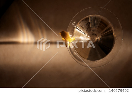Close-up view of a clear glass with a lemon twist garnish resting on a textured surface, soft lighting creating reflections and shadows around the glass Close-up view of a clear glass with a lemon twist garnish resting on a textured surface, soft lighting creating reflections and shadows around the glass 140579402