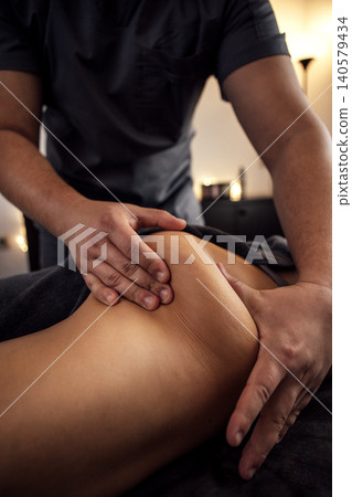 Male massage therapist performing therapeutic massage on a client's back in a serene spa environment, highlighting relaxation and wellness techniques for stress relief 140579434
