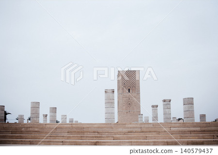 Historic stone columns surround a tall ancient tower under a cloudy sky, creating a serene atmosphere in a historical site with architectural significance and cultural heritage Historic stone columns surround a tall ancient tower under a cloudy sky, creating a serene atmosphere in a historical site with architectural significance and cultural heritage 140579437