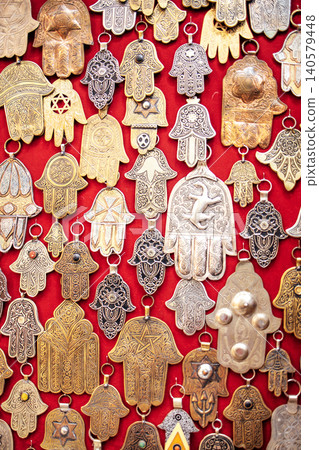Intricate collection of metallic hand-shaped amulets displayed on vibrant red fabric, showcasing cultural craftsmanship and artistic design elements in a decorative arrangement 140579448