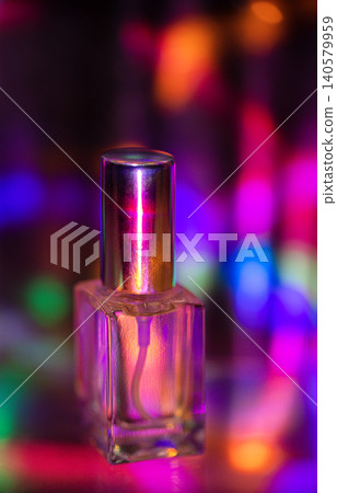 Transparent nail polish bottle with a metallic cap against a colorful bokeh background featuring vibrant pink, blue, green, and yellow lights creating a festive atmosphere Transparent nail polish bottle with a metallic cap against a colorful bokeh background featuring vibrant pink, blue, green, and yellow lights creating a festive atmosphere 140579959