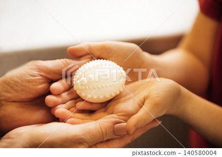 Adult and child hands exchanging a decorative white egg with pearl-like embellishments, soft focus background highlighting the act of sharing 140580004