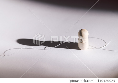 Wooden figure standing on white surface with shadow and string creating a visual path, minimalist composition emphasizing simplicity and form Wooden figure standing on white surface with shadow and string creating a visual path, minimalist composition emphasizing simplicity and form 140580025