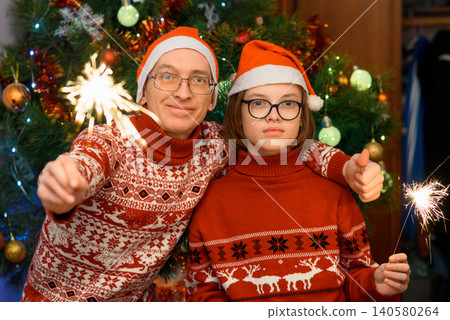 man shows a thumb up and a boy holds a sparkler near a christmas tree 140580264