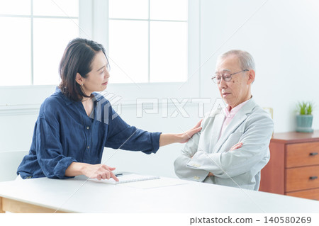 An elderly man writing in a notebook. 140580269