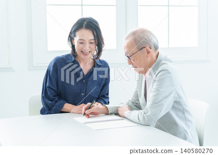 An elderly man writing in a notebook. 140580270
