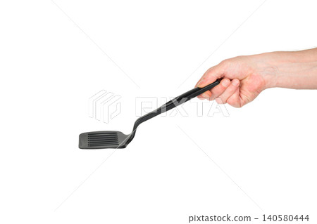 a hand holds a black plastic kitchen spatula horizontally from above on a white background a hand holds a black plastic kitchen spatula horizontally from above on a white background 140580444