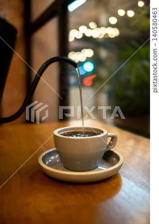 Warm Cafe Coffee Pouring Into White Ceramic Cup on Wooden Table 140580463