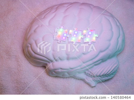 White brain-shaped model with three colorful puzzle pieces placed on top, set against a soft, textured background creating a unique conceptual visual White brain-shaped model with three colorful puzzle pieces placed on top, set against a soft, textured background creating a unique conceptual visual 140580464