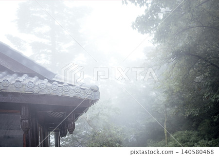 Traditional Asian architecture with ornate roof details partially obscured by misty forest landscape in a serene, tranquil environment Traditional Asian architecture with ornate roof details partially obscured by misty forest landscape in a serene, tranquil environment 140580468