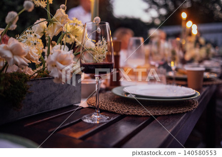 Elegant outdoor dining setup featuring a beautifully arranged table with floral centerpieces, wine glasses, and plates, creating a warm and inviting atmosphere for gatherings Elegant outdoor dining setup featuring a beautifully arranged table with floral centerpieces, wine glasses, and plates, creating a warm and inviting atmosphere for gatherings 140580553