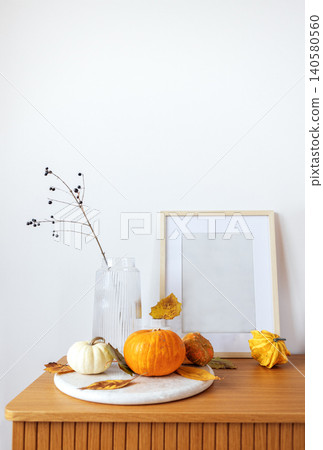 Decorative autumn arrangement featuring pumpkins, a glass vase with branches, and a blank picture frame on a wooden table, creating a cozy seasonal atmosphere with copy space Decorative autumn arrangement featuring pumpkins, a glass vase with branches, and a blank picture frame on a wooden table, creating a cozy seasonal atmosphere with copy space 140580560