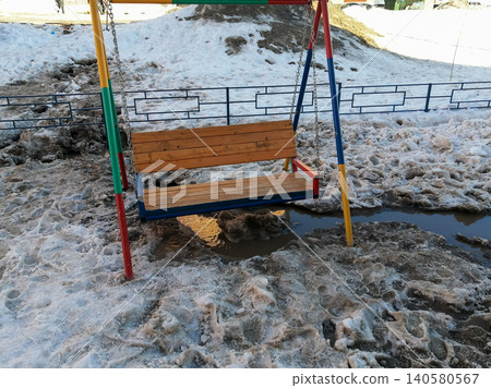 wooden swing on metal chains stands in the middle of melting snow and muddy puddles in spring wooden swing on metal chains stands in the middle of melting snow and muddy puddles in spring 140580567
