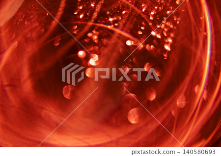 Abstract close-up of red liquid with bubbles and light reflections creating a vibrant, dynamic visual effect inside a transparent glass container 140580693