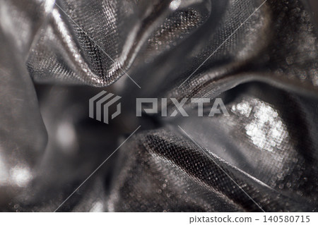 Close-up view of crumpled metallic silver fabric showcasing intricate texture and sheen, ideal for fashion, design, or textile applications Close-up view of crumpled metallic silver fabric showcasing intricate texture and sheen, ideal for fashion, design, or textile applications 140580715