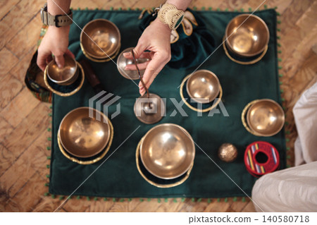 Hands of a person arranging various brass bowls and instruments on a green cloth, creating a serene atmosphere for meditation and mindfulness practices Hands of a person arranging various brass bowls and instruments on a green cloth, creating a serene atmosphere for meditation and mindfulness practices 140580718
