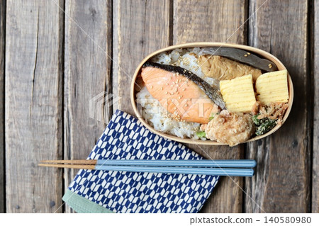 A Japanese bento box containing grilled salmon in a bentwood container, wrapped in a cloth with a Yagasuri (arrow feather) pattern. A Japanese bento box containing grilled salmon in a bentwood container, wrapped in a cloth with a Yagasuri (arrow feather) pattern. 140580980