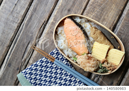 A Japanese bento box containing grilled salmon in a bentwood container, wrapped in a cloth with a Yagasuri (arrow feather) pattern. A Japanese bento box containing grilled salmon in a bentwood container, wrapped in a cloth with a Yagasuri (arrow feather) pattern. 140580983
